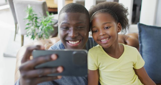 Image of african american father and daughter using smartphone. Enjoying quality family time together at home and using technology.