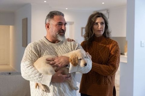 Middle-aged couple holding golden retriever puppy in cozy modern home knitwear