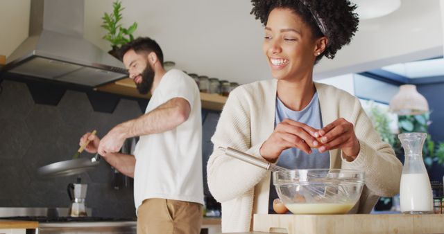 Image of happy diverse couple laughing and cooking breakfast in kitchen, with copy space. Happiness, inclusivity, free time, togetherness and domestic life.