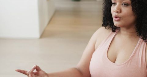 Curly-haired woman practicing mindful breathing on wood floor in minimalist interior