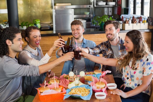 Group of friends enjoying a casual meal and drinks in a pub, toasting with beer bottles and soda. Ideal for use in advertisements for restaurants, pubs, social events, and lifestyle blogs. Perfect for illustrating themes of friendship, celebration, and social gatherings.
