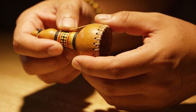 Close-up of hands holding handcrafted leather gourd shaker with woven bead detail, rustic
