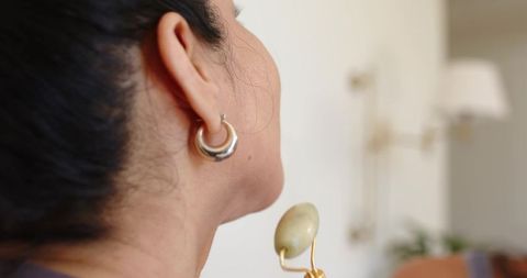 African american woman massaging jaw with green jade roller wearing double hoop earrings