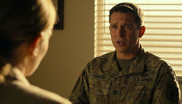 U.s. Army sergeant speaking to colleague in office showing uniform patches and rank, by window blind