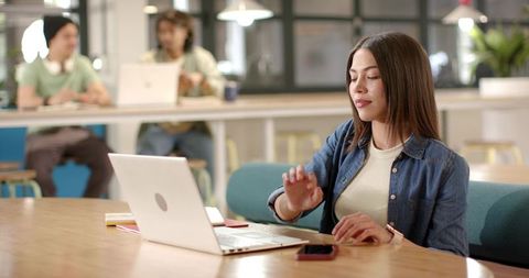 Young African American woman typing on laptop in modern coworking space with colleagues