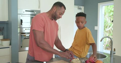 African american father and son preparing healthy snack together on kitchen island