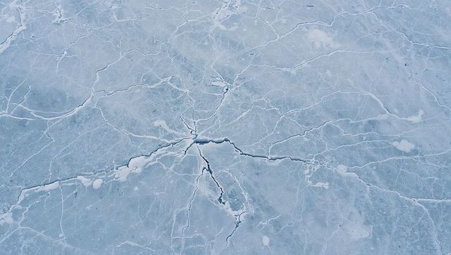 Star-shaped ice fracture radiating across frozen lake revealing intricate crack network