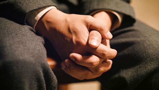 Clasping hands resting on lap in suit closeup conveying professional tension and focus