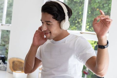 Young man dancing, listening to music on wireless headphones in sunlit kitchen