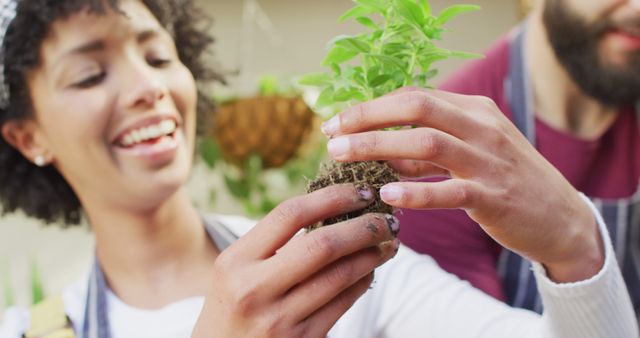 Smiling young woman gently planting herbs with hands covered in soil. Perfect for depicting sustainable living, gardening interests, nature activities, outdoor hobbies, teamwork, and eco-friendly practices. Ideal for use in gardening blogs, lifestyle magazines, environmental campaigns, and educational content about horticulture.