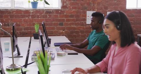 Typing professionals wearing headsets in open-plan office collaborating in modern workspace