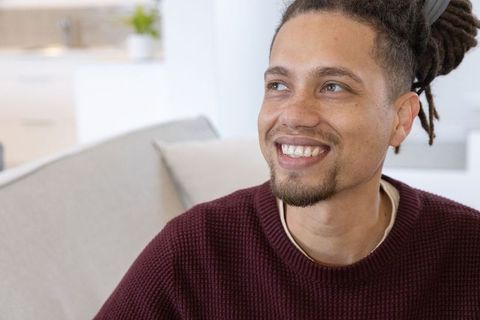 Smiling african american man with dreadlocks wearing maroon sweater in cozy living room
