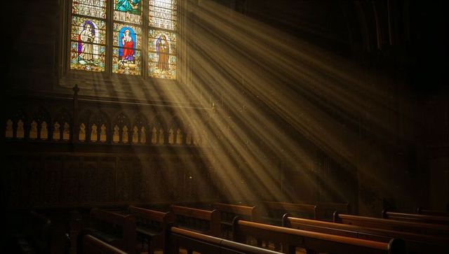 Golden sunbeams streaming through stained glass into gothic cathedral nave, dust motes
