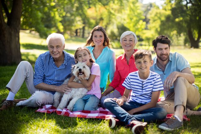 Multigenerational family enjoying a sunny day in the park, sitting on a picnic blanket with their dog. Ideal for use in advertisements, family-oriented content, lifestyle blogs, and promotional materials highlighting family bonding, outdoor activities, and leisure time.
