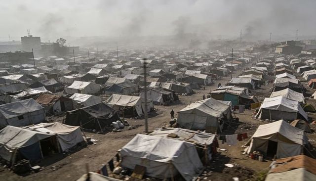 Sprawling tent camp on dusty outskirts showing overcrowded makeshift shelters and smoke