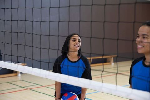 Diverse teen volleyball players practicing indoors holding tricolor ball at net