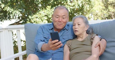 Senior couple browsing smartphone on porch, relaxing together and sharing memories outdoors