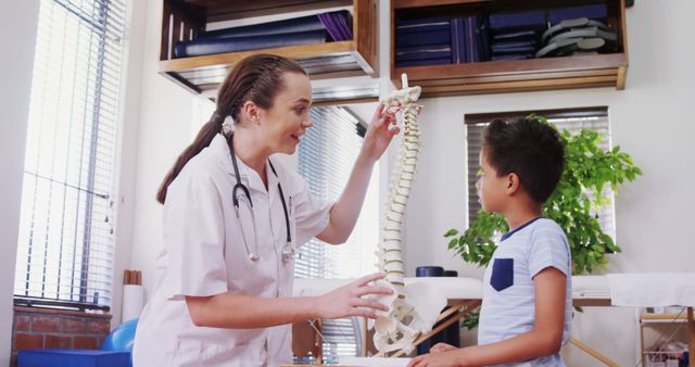 This image depicts a compassionate pediatrician using a spinal model to explain spine anatomy to a young boy in a clinic. Ideal for use in healthcare materials, educational resources, and pediatric clinic promotions.