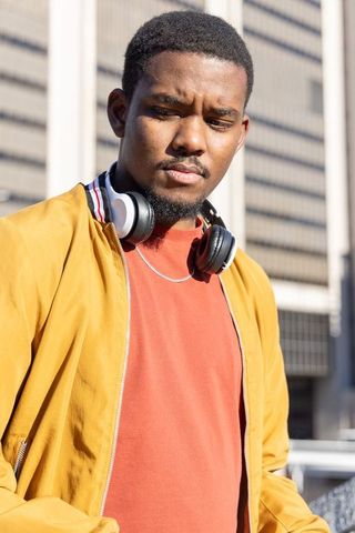 African american man squinting in sunlight wearing mustard jacket and over-ear headphones