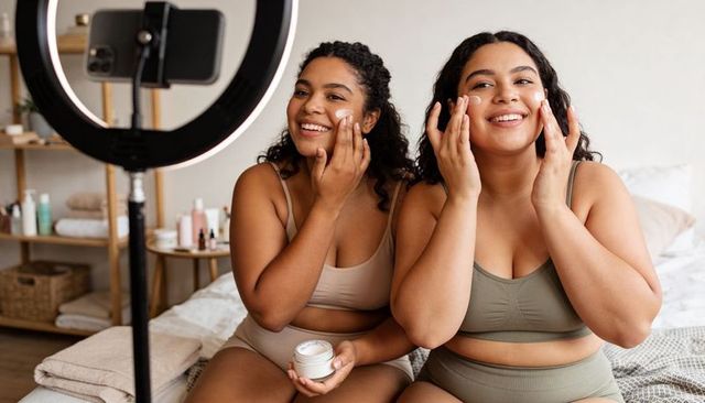 Smiling plus-size women applying moisturizer while filming beauty tutorial with ring light