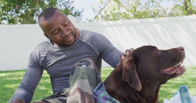 African american male soldier sitting and petting his dog in garden. Patriotism, army and returning home concept.