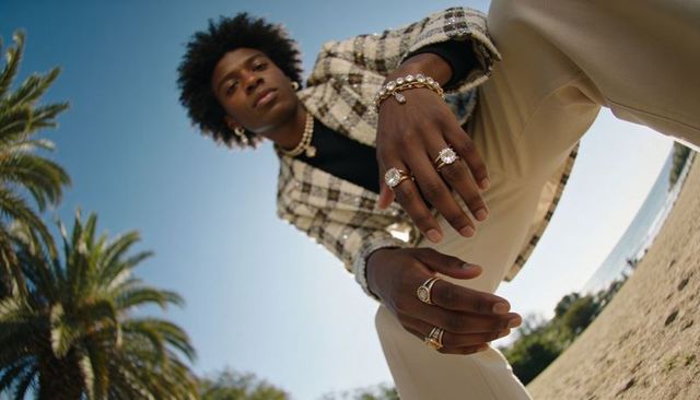 Crouching male model showcasing luxury rings and bracelets on sunny beach fashion portrait