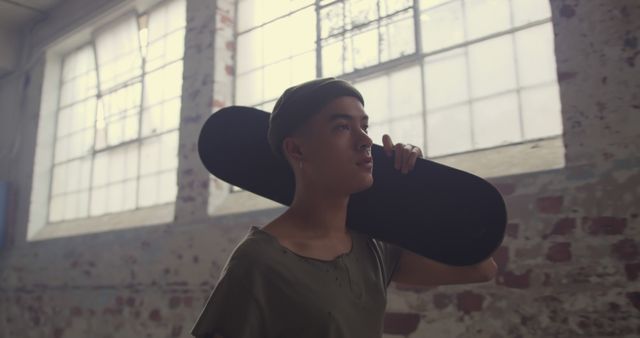 Urban Teen Holding Skateboard in Industrial Warehouse - Download Free Stock Images Pikwizard.com