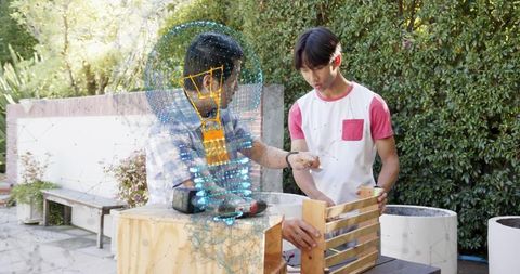 Mentor guiding teen assembling wooden crate using augmented reality drill outdoors