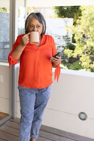 Senior woman relaxing on balcony with coffee and smartphone