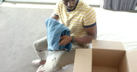 Man packing shirt into box in sunlit bedroom setting