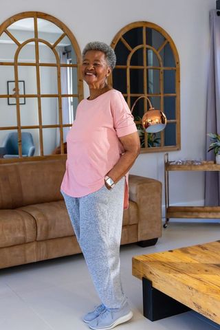 Smiling senior african woman standing with hands in pockets in modern living room