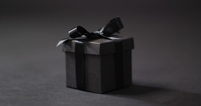 Black gift box with black ribbon on dark grey background with copy space. Luxury treat, present, shopping, black friday sale and retail concept digitally generated image.