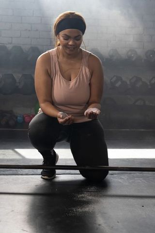 African american athlete kneeling chalking palms preparing for barbell lift in gym