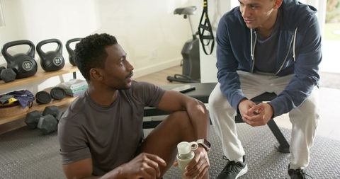 Diverse personal trainer coaching client while resting after workout in home gym