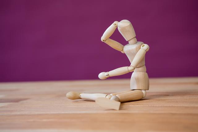 Wooden art mannequin performing a stretching exercise on a wooden surface with a purple background. Ideal for illustrating concepts of flexibility, health, fitness, relaxation, and creativity. Useful for art projects, fitness blogs, wellness articles, and educational materials.
