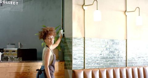 Smiling barista adjusting light switch in cozy modern cafe with tiled wall and booth