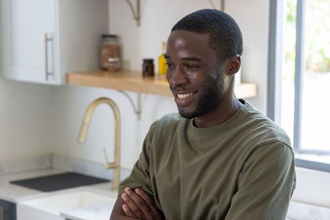 African american man standing in modern kitchen smiling with arms crossed near sink