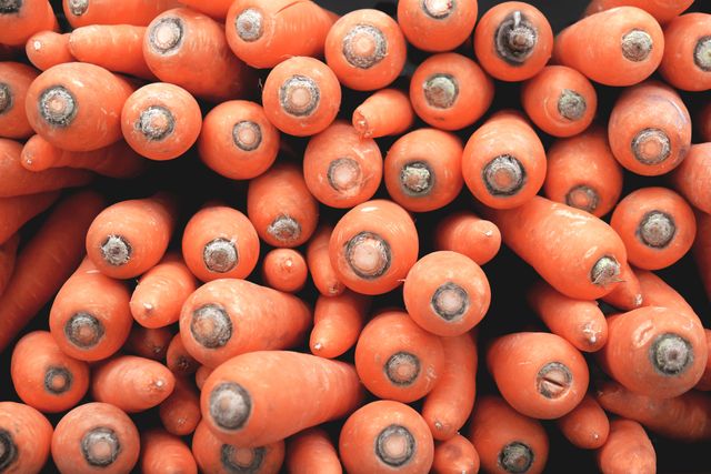 A vibrant display of fresh organic carrots piled in a market stall. The bright orange vegetables seem freshly harvested, evident through their crisp appearance. Suitable for agriculture-themed content, articles about healthy eating, or anything related to vegan and natural diets.