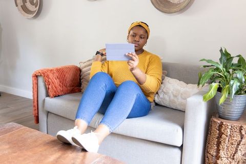 Young african american woman relaxing on sofa using tablet in cozy modern living space