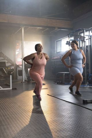 Two diverse women performing synchronized forward lunges in industrial-style gym