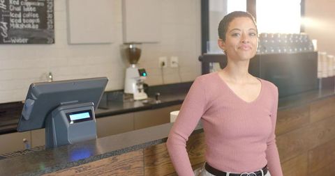Confident barista smiling and working behind modern cafe counter with pos terminal