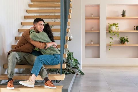 Young couple embracing on floating wooden stairs in modern minimalist home interior