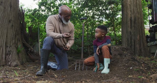 Grandfather kneels beside grandson in a garden, demonstrating planting technique. Excellent for depicting family bonding, outdoor learning activities, and intergenerational knowledge transfer. Suitable for educational materials, gardening blogs, and family-oriented content.