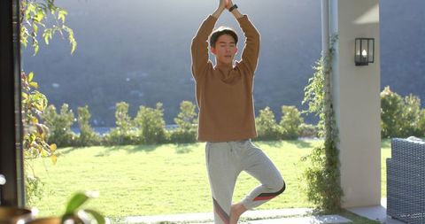 Asian Man Practicing Yoga Tree Pose on Sunny Patio