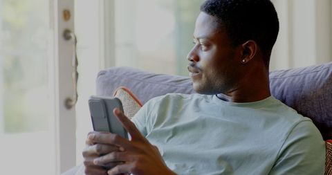 Man Relaxing with Smartphone by Window at Home