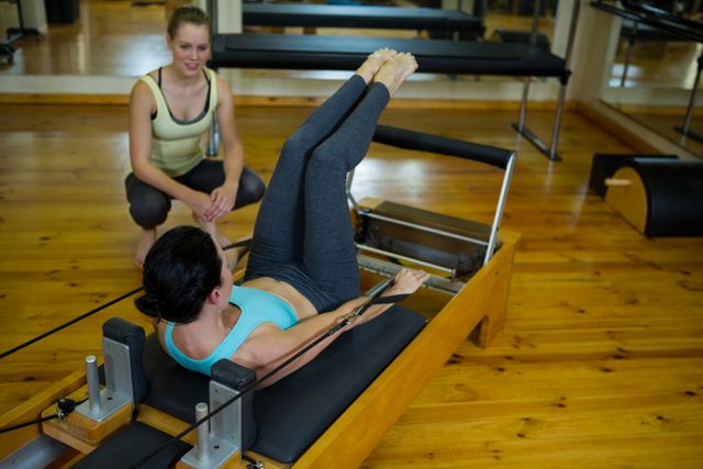 Female trainer assisting woman with stretching exercise in gym