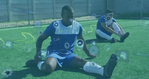 Soccer players stretching on artificial turf during outdoor training with agility hurdles