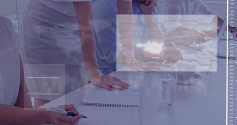 Office team leaning over table discussing documents with laptop, notebook and pen