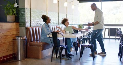 African american friends chatting over coffee at sunlit cafe banquette sharing smartphone