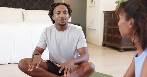 African american couple sitting and talking on yoga mat in minimalist bedroom for wellness
